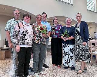 Eine Gruppe von sieben Personen posiert in einem hellen Raum.
