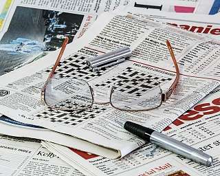 Eine Brille und ein Stift liegen auf Zeitungsseiten mit Kreuzworträtseln.