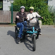 Zwei Personen sitzen auf einem Lastenrad in einer urbanen Umgebung.