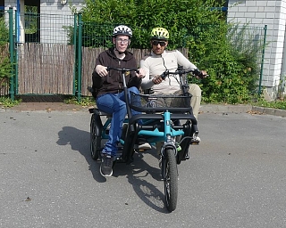 Zwei Personen sitzen auf einem Lastenrad in einer ruhigen Umgebung.