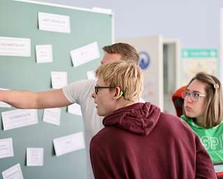 Schüler diskutieren an einer Tafel mit Beschriftungen.