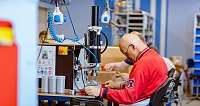 Mitarbeiter montiert Teile an einer Maschine in einer Produktionshalle.
