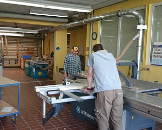 Zwei Personen arbeiten in einer Holzwerkstatt mit Maschinen.