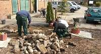 Drei Arbeiter legen Steine in einem Gartenbereich.