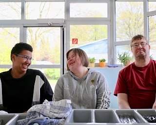 Drei Personen sitzen in einem hellen Raum und lachen.