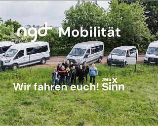 Eine Gruppe von Menschen steht vor mehreren weißen Transportern.