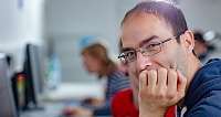 Ein Mann mit Brille lächelt, während er an einem Computer sitzt.