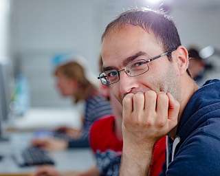 Ein Mann mit Brille lächelt, während er an einem Computer sitzt.