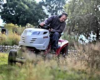 Mann mäht Gras mit einem Rasenmäher im Garten.