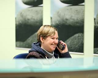 Frau spricht lächelnd am Telefon an einem Empfangstresen.